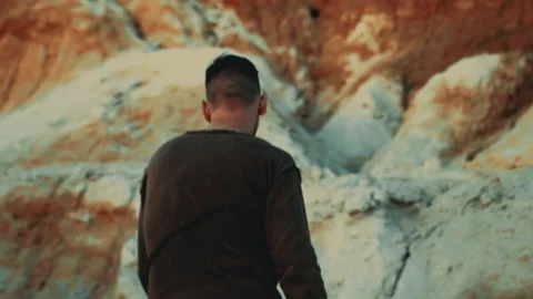 A man walks along a sandy, dried-up valley against the background of rocks. Stock Footage 160508698