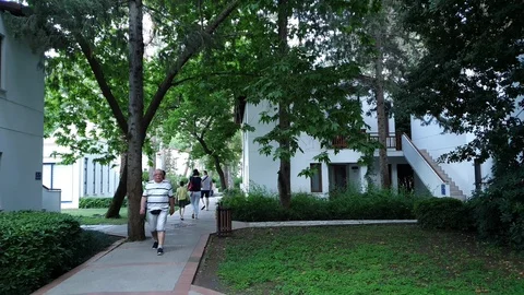 Man walks along small resort park with trees and houses Stock Footage 110990716