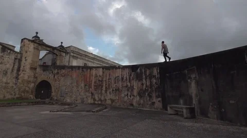Man Walks Along Top of an Old Exotic Concrete Wall Stock Footage 79276609
