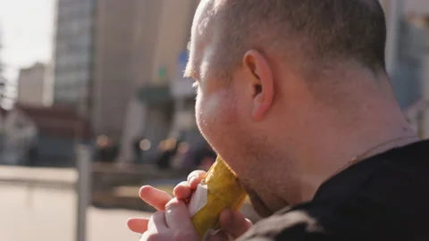 A Man Walks and Eats Kebab on a City Street. Hungry Person in Black T-shirt Stock Footage 234504261