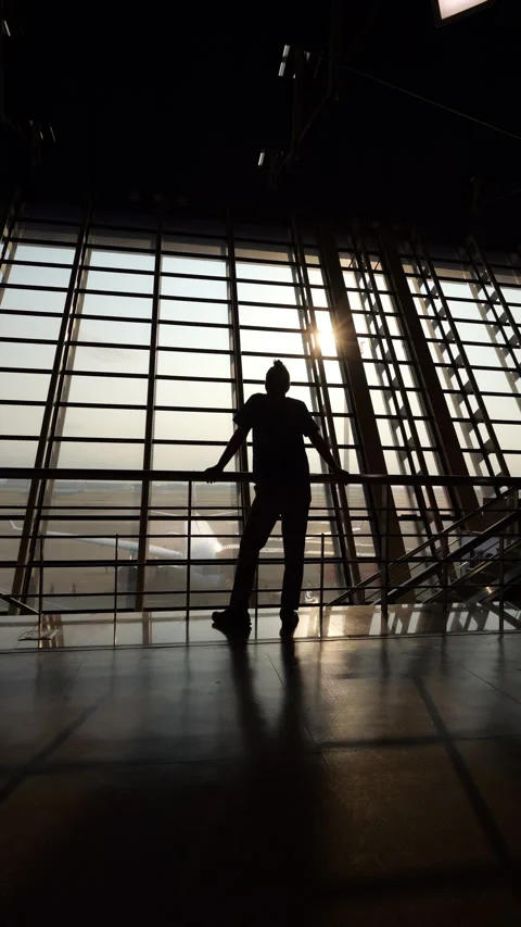 Man walks and stands looking at airplane from the terminal window, silhouetted Stock Footage 297055359