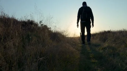 Man walks away from camera on grassy path at sunset Stock Footage 293942513
