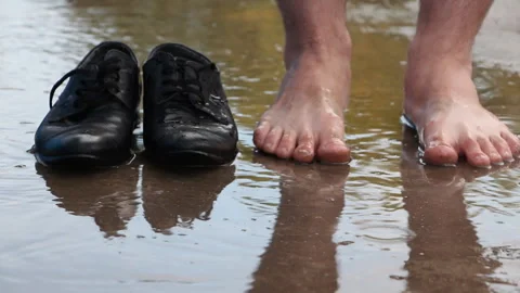 A man walks barefoot through a puddle and throws his shoes near him Stock Footage 111256954