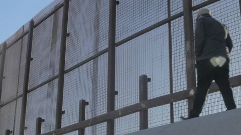 Man Walks Casually Along the US and Mexico Border Fence Stock Footage 60632080