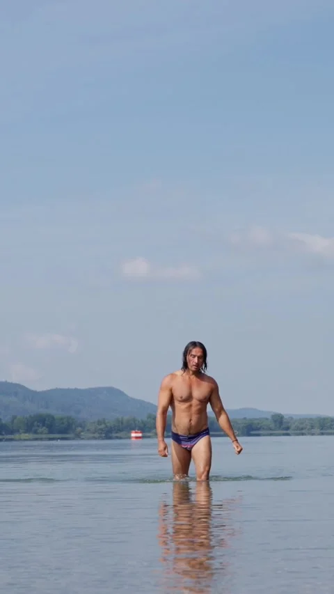 A man walks with confidence through clear, shimmering water on a bright sunny Stock Footage 317268078