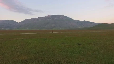 A man walks in a desert valley surrounded by the Italian Apennines. Aerial Stock Footage 70952065