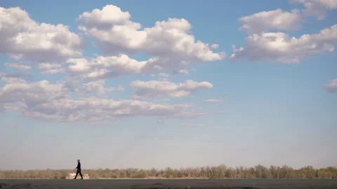 A man walks in the distance.In background is forest and a cloudy beautiful sky Stock Footage 130727592