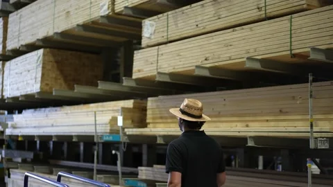 Man walks down aisle with stacks and piles of lumber, wood, and sheets of Video stock 158379068