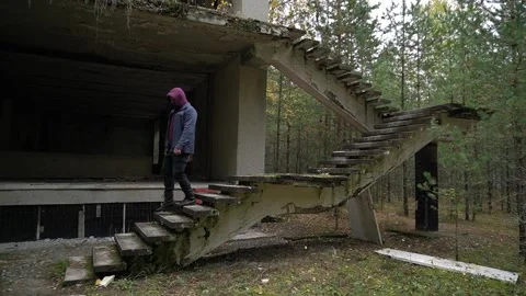 Man walks down a broken staircase along an abandoned house. autumn gloomy Stock Footage 288793016