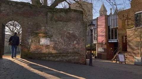 Man walks down cobbled lane into a walled garden near the Abbey 動画素材 120689018
