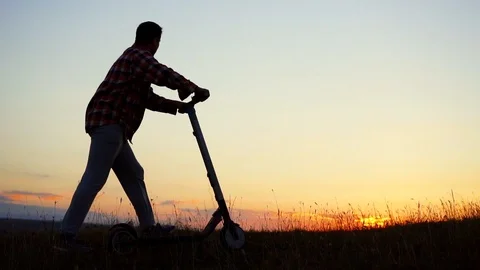 Man walks down the hill with an electric scooter and watches the sunset,slow mo Stock Footage 95865627