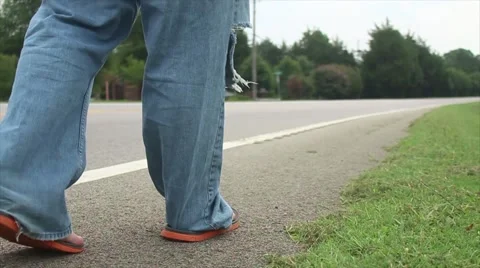 Man Walks Down Side Of The Road In Tattered Jeans Stock Footage 53090389