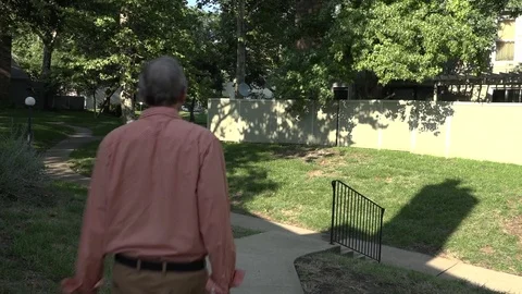 A Man Walks Down a Sidewalk and a Set of Stairs Through Grassy Area of Townhomes Stock Footage 79111013