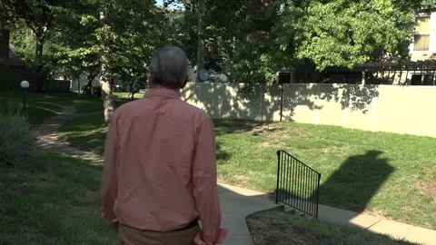 A Man Walks Down a Sidewalk and a Set of Stairs Through Grassy Area of Townhomes Stock Footage 79111072