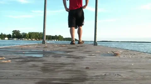Man Walks to End of Dock and Sits Video stock 12598955