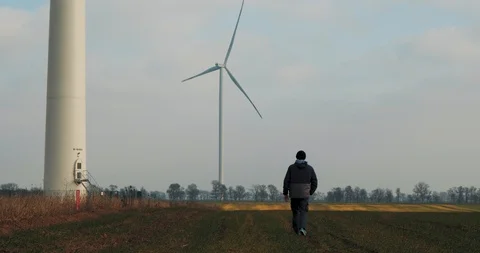 A man Walks In A Field On Background Rotating Windmill. The Power Of The Wind Stock Footage 123712178