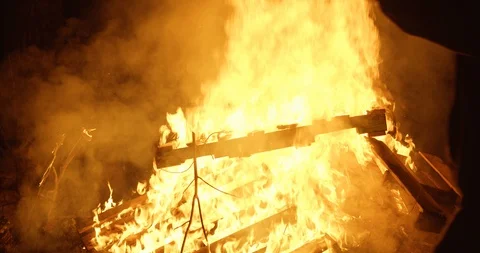 Man walks in front of large bonfire holding a skid palette then throws it on Stock Footage 122076844