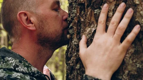 A man walks up to a huge tree, sniffs the bark and hugs the trunk. An adult m Vídeos de archivo 172283328