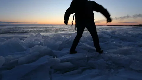 A man walks on the ice on the shore of the lake during the sunrise. Stock Footage