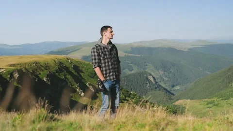 Man walks on a mountain meadow with green hills and valleys in the background on Stock Footage 343840405