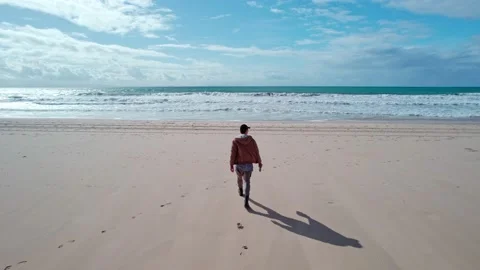 A man walks to the ocean on the beach Stock Footage 231221379