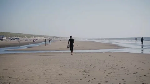 A man walks on an ocean beach full of people on a sunny day Vídeo Stock 197045761