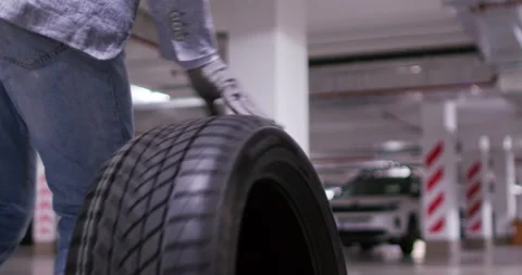 Man walks parallel to rolling tire guiding rubber with hand Stock Footage 294611062