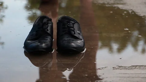 A man walks on a puddle on the pavement, stops and moves off his shoes Stock Footage 108443931