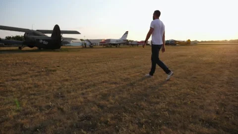 Man in walks purposefully across an open field, surrounded by aircraft Stock Footage 321770580