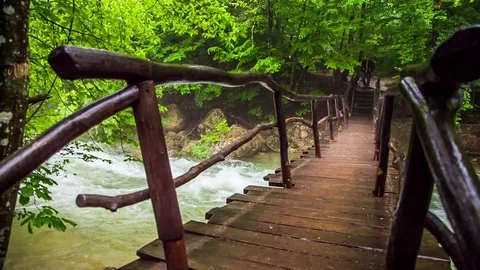A man walks in the rain over a bridge over a mountain river Video stock 79979821