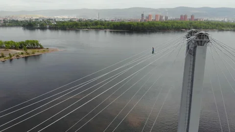 A man walks on a rope stretched between the supports of the bridge at high Stock Footage 113135804