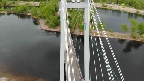 A man walks on a rope stretched between the supports of the bridge at high Stock Footage 113136426