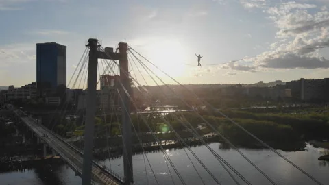 A man walks on a rope stretched between the supports of the bridge at high Video stock 113140039