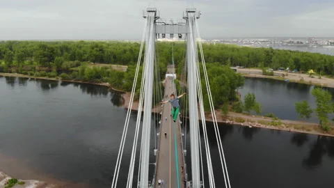 A man walks on a rope stretched between the supports of the bridge at high Stock Footage 113146280