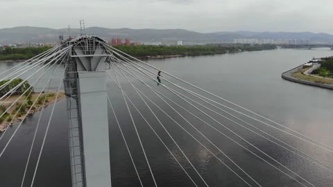 A man walks on a rope stretched between the supports of the bridge at high Video stock 113146440