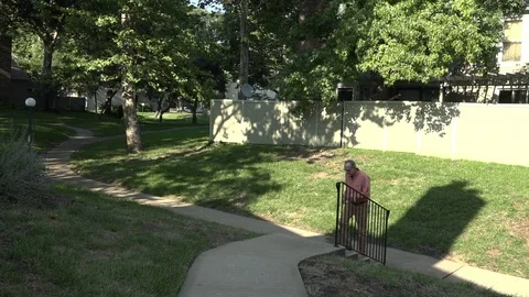 A Man Walks up a Sidewalk and a Set of Stairs Through Grassy Area of Townhomes Stock Footage 79111014