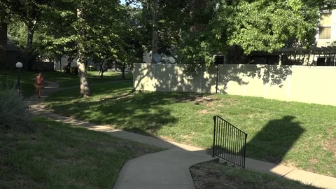 A Man Walks up a Sidewalk and a Set of Stairs Through Grassy Area of Townhomes Stock-Footage 79111085
