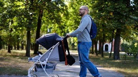 Man walks with a stroller in the park. Caring father for a walk with a child Stock Footage 118690605