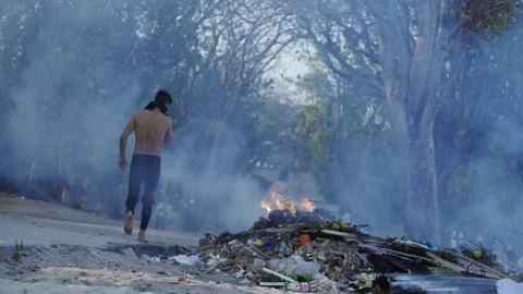 Man Walks Through Burning Plastic Trash on the Streets in Bali Environment Stock Footage 119904286