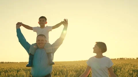 A man walks through a field with wheat with a small son child on his shoulders Stock Footage 248418089