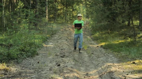 A man walks through the forest with a laptop and looking map He chooses the Stock Footage 65014392