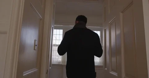 A man walks through a hallway of a nice home to a window Stock Footage 73251439