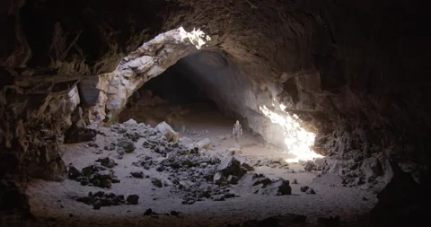 Man walks through light of giant cave and stands on caved in rocks wide Stock Footage 220906331