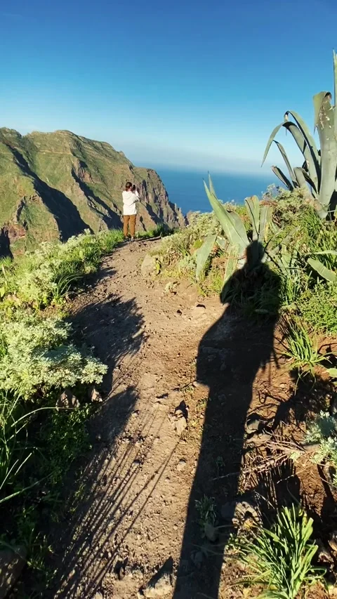 Man walks towards path at top of mountain. Sun is shining and shadow from the 動画素材 156804232