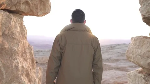 Man walks under a stone monument in a desert sunrise Stock Footage 73080275