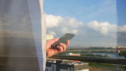A man walks to window, in his hand is telephone. From window overlooking city. Stock Footage 106000877