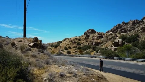 Man wanders alone along road in California desert mountains above Yucca Valley Video stock 116985552