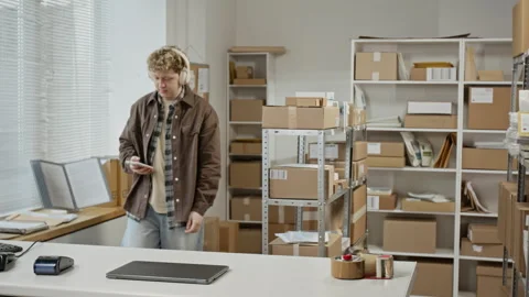 Man in Warehouse Opening Laptop to Manage Ecommerce Orders Stock Footage 342589778