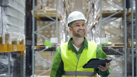 Man warehouse worker walks through rows of storage racks with merchandise and Video stock 124451714