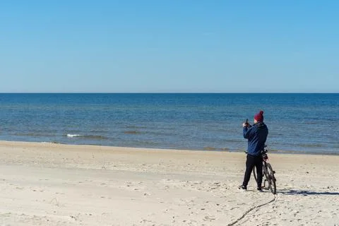 A man in warm clothes and a hat takes a photo on his phone standing near hi.. Stock Photos